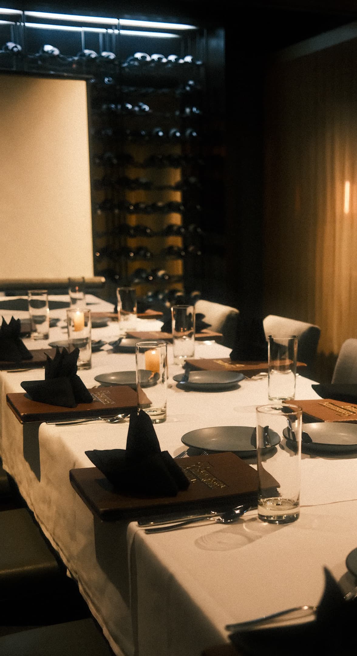 A long table set for a private dinner Upstairs, with menus at every place and the wine wall behind