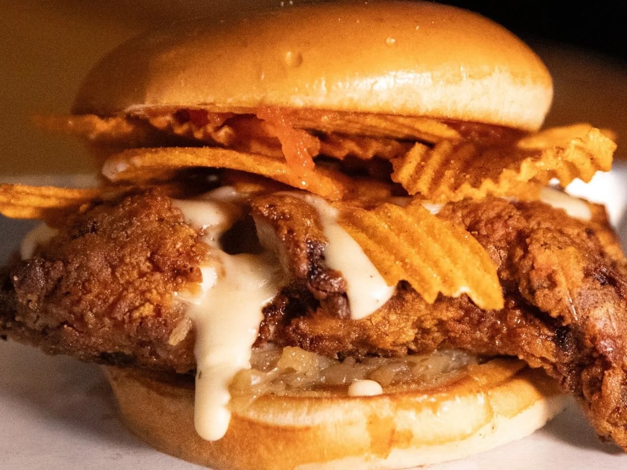 A Byrd & Barrel fried chicken sandwich topped with sauce and crisp chips